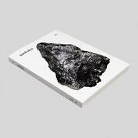 A side view of Sankaku Vol 3: GODS book, published by Sankaku and on show at NiMi Projects UK. The cover is white with a photographic image of a large, naturally formed, grey triangular rock.