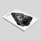A side view of Sankaku Vol 3: GODS book, published by Sankaku and on show at NiMi Projects UK. The cover is white with a photographic image of a large, naturally formed, grey triangular rock.
