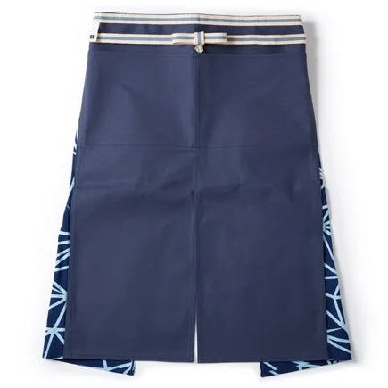  A contemporary take on the traditional maekake Japanese apron with a blue sailcloth canvas front panel, two pockets, patterned tenugui cotton and a sanada himo double wrap woven waist cord. Made in Japan, available at NiMi Projects UK.
