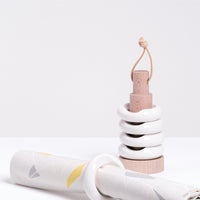 Five Ceramic Japan white hashioki chopstick rests, all ring shaped with an indent — 4 are stacked on a wooden pole stand with a leather strap at the top, the fifth is in front serving as a napkin holder. On display at NiMi Projects UK