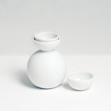 Kaichiro Yamada's white porcelain Snowman Sake set, featuring a rotund sake bottle and two hemisphere cups, one slotted inside the lip of the bottle, the other by its side.  Made in Japan, photographed by NiMi Projects UK