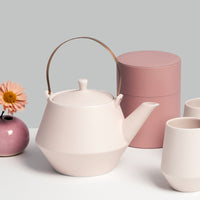 Frustum porcelain teapot with brass handle and matching cups in off-white, designed and made in Japan, with a pink Moheim tin canister and pink Okada bud vase in a photo by NiMi Projects UK