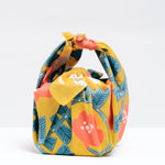 A Musubi Hummingbird pattern Japanese furoshiki wrapping cloth used to wrap a cube-shaped package by NiMi Projects UK