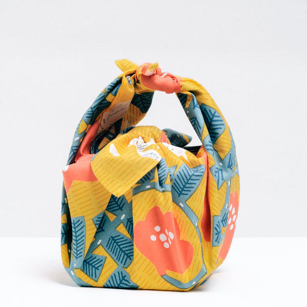 A Musubi Hummingbird pattern Japanese furoshiki wrapping cloth used to wrap a cube-shaped package by NiMi Projects UK