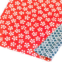 A Musubi Japanese furoshiki wrapping cloth, featuring a pattern of apricot flowers on a red background on one side and a geometric pattern of bamboo and pine bark in white on navy blue on the other side. Made in Japan and available at NiMi Projects UK
