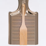 A gold coloured aluminium oroshigane Japanese grater, made in Japan by Nanmoku, paired with a bamboo scraping brush and available at NiMi Projects UK.