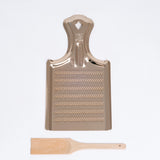 A gold colored aluminum Nanmoku oroshigane Japanese grater, paired with a bamboo scraping brush, made in Japan and available at NiMi Projects UK.