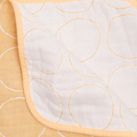 A close up of the reverse side of a yellow NiMi Projects' Blanked Japanese gauze cotton blanket showing a white background with yellow circles.