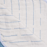 A closeup of one side of a blue reversible Blanked Japanese cotton gauze blanket, featuring a white background with a woven pattern of blue lines — available at NiMi Projects UK. 