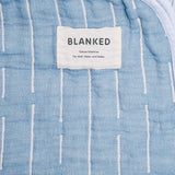 A closeup of a NiMi Projects' blue Blanked Japanese cotton gauze blanket, featuring the Blanked label and a pattern of woven white lines.