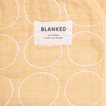 A closeup of a Blanked Japanese cotton gauze blanket in yellow with a woven pattern of white circles, featuring the Blanked design label, available at NiMi Projects UK.