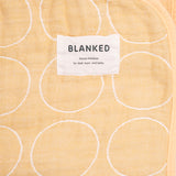 A closeup of a Blanked Japanese cotton gauze blanket in yellow with a woven pattern of white circles, featuring the Blanked design label, available at NiMi Projects UK.