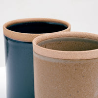 A detail shot of two NiMi Projects Sakuzan Mino-yaki Japanese porcelain Straight Mugs (left in navy blue, right in beige), showing their unglazed lips revealing the color and texture of the clay.
