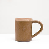 A Japanese porcelain Straight Mug with an extra wide, rounded handle, made in Gifu by Mino-yaki ceramicists Sakuzan. The mug's body is beige brown, while its lip is left unglazed, revealing the natural color and texture of the clay.  