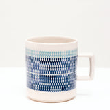 Pottery artisan Yoji Sone's Japanese porcelain white Kanna Mug, decorated with a wide band of navy blue glaze topped with a strip of pale blue. The glazes are punctuated by tiny indents, a traditional ceramics technique called tokibaanna. Available t NiMi Projects UK, 