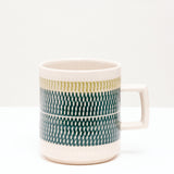 A NiMi Projects' Mino-yaki, Japanese porcelain white Kanna Nug, glazed with a wide band of dark green, topped with thinner shallow band of pale green, designed by pottery artisan Yoji Sone. The mug's bands of color are textured with tiny indented marks using a pottery technique called tokibanna.