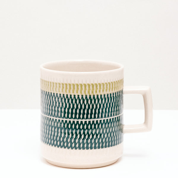 A NiMi Projects' Mino-yaki, Japanese porcelain white Kanna Nug, glazed with a wide band of dark green, topped with thinner shallow band of pale green, designed by pottery artisan Yoji Sone. The mug's bands of color are textured with tiny indented marks using a pottery technique called tokibanna.