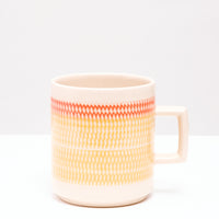 A NiMi Projects' yellow and orange Kanna Mug made of Mino-yaki Japanese porcelain and designed by pottery artisan Yoji Sone. The mug's wide band of yellow topped with a thinner band of orange are textured with tiny indented marks using a technique called tokibanna, 