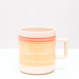 A NiMi Projects' yellow and orange Kanna Mug made of Mino-yaki Japanese porcelain and designed by pottery artisan Yoji Sone. The mug's wide band of yellow topped with a thinner band of orange are textured with tiny indented marks using a technique called tokibanna, 