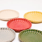 A Closeup view of five NiMi Projects' Japanese Hana Akari Mino-yaki porcelain chrysanthemum dishes, showing their radially fluted pattern. Colors, clockwise from bottom left — grey, white, yellow, green and red in the center.