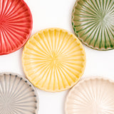 A close up image of five NiMi Projects' Hana Akari Japanese porcelain chrysanthemum plates, in different colors. Clockwise from top right — red, green, white, grey and yellow in the center.