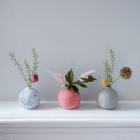 Three rotund Moheim Color Drops bud vases in white with blue flecks, coral red with white flecks and gray with white flecks, each holding a sprig of flowers, designed in Japan and available at NiMi Projects UK.