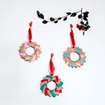 Three origami Christmas wreaths - one in pink, gold and tan, one in blue, gold and tan, and another in red, green and tan - all topped with red ribbon trimmed in gold. Handmade at NiMi Projects UK with Japanese origami paper.