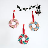 Three origami Christmas wreaths - one in pink, gold and tan, one in blue, gold and tan, and another in red, green and tan - all topped with red ribbon trimmed in gold. Handmade at NiMi Projects UK with Japanese origami paper.