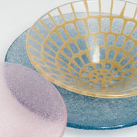 Close up image of a yellow mosaic Afumi glass fruit bowl, placed atop a blue-purple Shari Shari frosted glass platter, both alongside a pink Shari Shari bowl — all made by Japanese glass artisan Saburo and available at NiMi Projects.