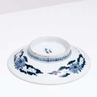 The bottom of a 1940s vintage Japanese white Arita Porcelain plate, featuring a design of blue lotus flowers and leaves and small stripes on the base. Available at NiMi Projects UK