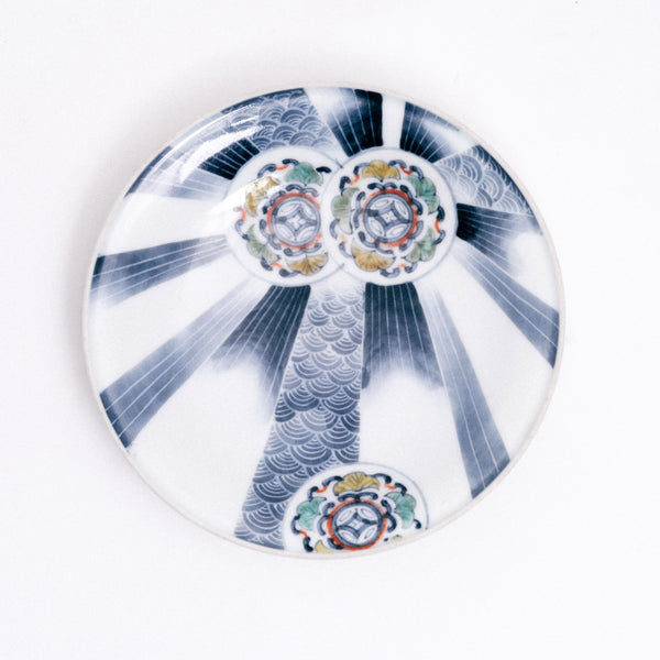 A 1940s vintage Japanese Arita blue and white porcelain plate featuring a design of three circles with arabesque patterns and leaves, and rays of gradient blue stripes and arched wave patterns, on display at NiMi Projects UK