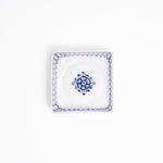 A NiMi Projects vintage Japanese blue and white porcelain square dish featuring a central blue flower design and decorative striped details on the inside rim.