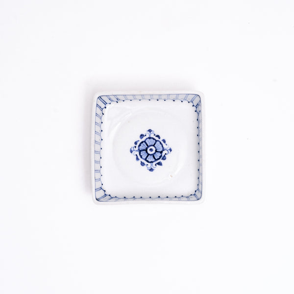 A NiMi Projects vintage Japanese blue and white porcelain square dish featuring a central blue flower design and decorative striped details on the inside rim.