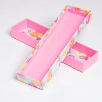  An open Yuzen Washi Pen Box, made of traditional chiyogami Japanese washi paper, featuring a bright pink interior, with an outside and inner wrapping of patterned washi paper with pink, orange and yellow flowers on a blue background. Available at NiMi Projects UK.