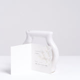 Ceramic Japan's white porcelain tubular Jam Jar vase, shaped  in the silhouette of a jar and on display with a gift card as one of the brand's Still Green series at NiMi Projects UK.