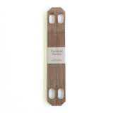 A pair of Patchin walnut wood accessories to turn a furoshiki wrapping cloth into a bag on sale at NiMi Projects.