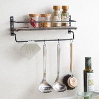 A silver Japanese irogami kitchen grater hanging on a kitchen spice shelf, with silver ladles and a brush hanging next to it and bottles of spice lined up above.