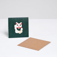 A square Japanese Motif Mini Card, featuring a picture of a white manekineko lucky cat on a green background, with a brown envelope. Printed in Japan and available at NiMi Projects UK.