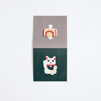 A square Japanese Motif Mini Card, printed in Japan and available at NiMi Projects UK, featuring an illustration of a white manekineko lucky cat on a green background on one side and a yellow uchide no kozuchi lucky mallet on a grey background on the other.