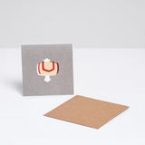 A square Japanese Motif Mini Card, featuring an illustration of a yellow uchide no kozuchi lucky mallet on a grey background, with a brown envelope. Printed in Japan and available at NiMi Projects UK.