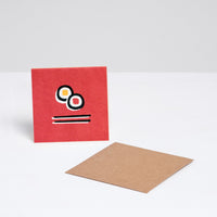 A square Japanese Motif Mini Card, featuring a picture of two norimaki sushi rolls and a pair of chopsticks on a red backround, with a brown envelope. Printed in Japan and available at NiMi Projects UK.