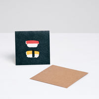 A square Japanese Motif Mini Card, featuring a picture of two pieces of nigiri sushi on a black background, with a brown envelope. Printed in Japan and available at NiMi Projects UK.