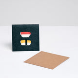A square Japanese Motif Mini Card, featuring a picture of two pieces of nigiri sushi on a black background, with a brown envelope. Printed in Japan and available at NiMi Projects UK.