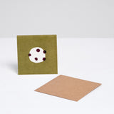 A square Japanese Motif Mini Card, featuring a picture of a shiroi daifuku (white mochi cake dotted with black beans) on a green background, with a brown envelope. Printed in Japan and available at NiMi Projects UK.