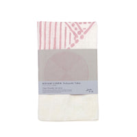 A white linen Musubi furoshiki with a red geometric design by Nobuyuki Takai, folded and wrapped with a paper label, available at NiMi Projects UK.
