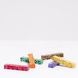 Six Japanese Aozora Dot crayons, each rectangular and composed of a mosaic of different colored wax, laid out randomly at NiMi Projects UK. 