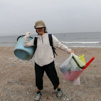 A member of Buoy carrying a bucket and bag of other plastic waste found on the shores of Japan to be recycled into home items.