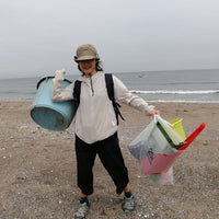 A beach ocean plastic waste collector, holding a bucket and bag of other plastic objects collected from a shore in Japan to be recycled into Buoy products.