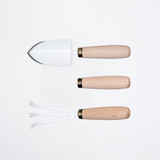 The Asano Mokkousho Mini Gardening set of white enameled tools with rounded  snow  beech handles, laid out from  top to bottom — a trowel, a pick or dibble, a claw-like fork.  All made in stainless steel in the Tsubame-Sanjo metalworking district, and with sustainable wood,  sourced in Niigata. Available at NiMi Projects UK.