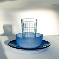 A display of vintage Japanese blue glass, featuring a window-paned glass inside a frosted blue bowl, on top of a deep blue plate.